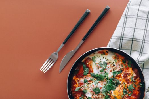 Top view of a vibrant shakshouka dish with fork and knife on an orange table, perfect for food photography.