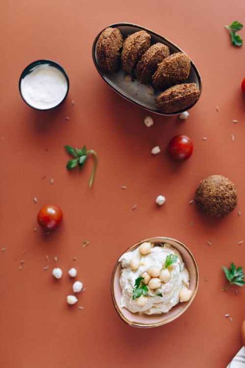 Free Flat lay of falafel and hummus on orange background with cherry tomatoes and sauce. Stock Photo