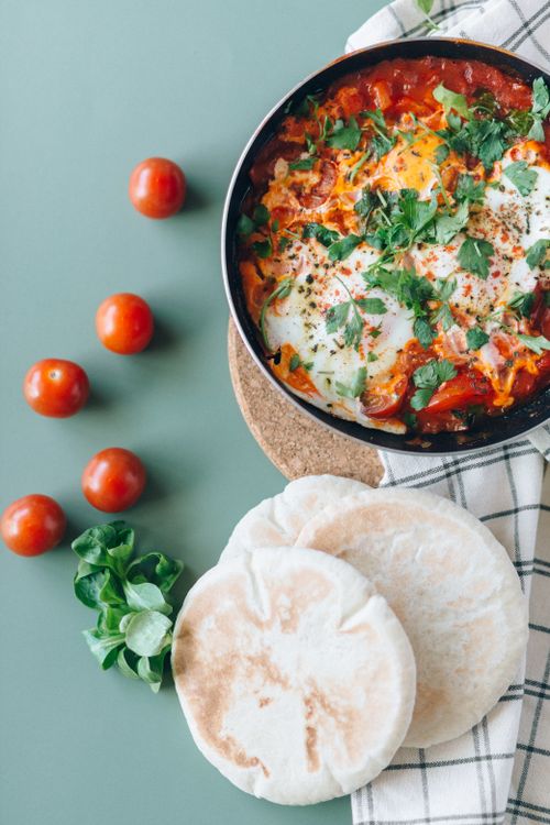Free Top view of shakshuka with pita bread on a green table, garnished with herbs. Stock Photo