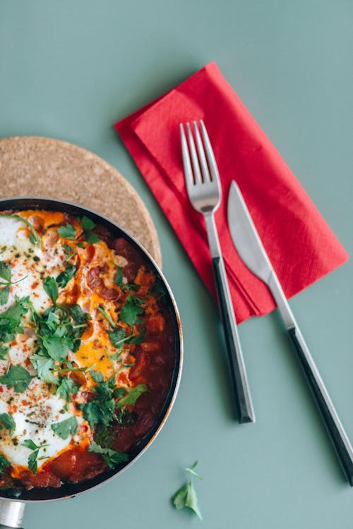 Free Stainless Steel Fork and Knife Besides a Shakshouka Plate Stock Photo