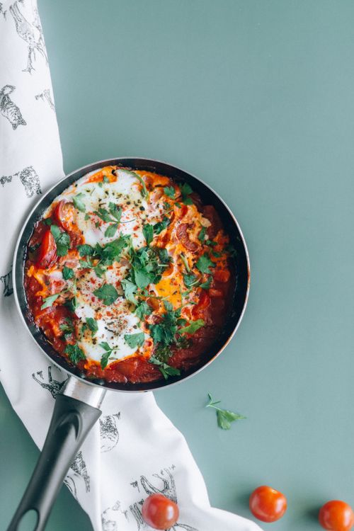 Free A vibrant pan of shakshuka with tomatoes and herbs on a pastel background. Stock Photo
