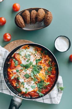 Mouth-watering shakshuka with eggs, parsley, and falafel on a green tabletop.