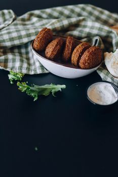 A close-up of falafel in a bowl with sauce and greens on a dark table.