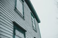 Low angle of aged building exterior with painted wooden wall and shutters under light sky in town