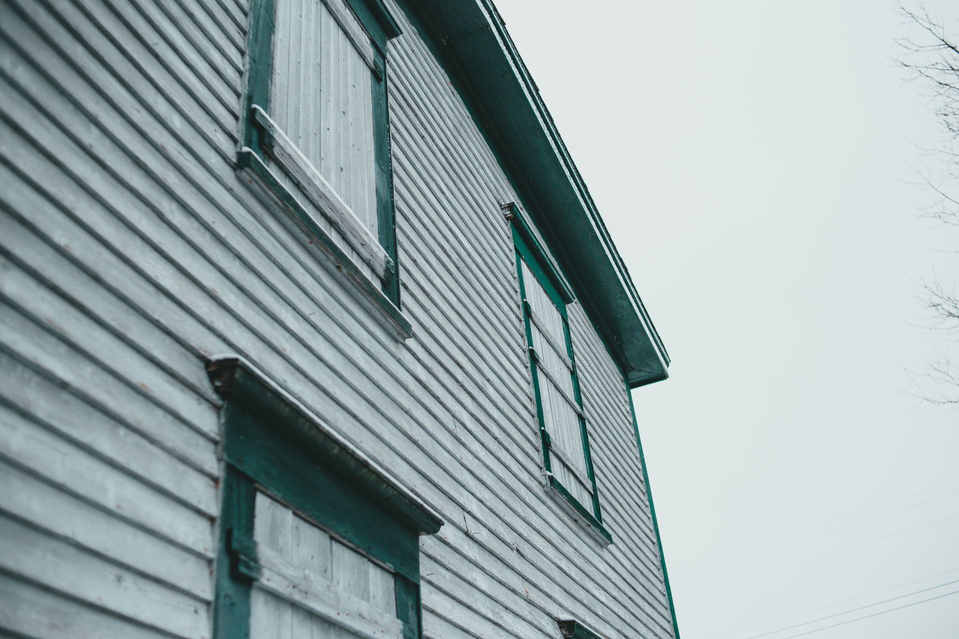 Low angle of aged building exterior with painted wooden wall and shutters under light sky in town