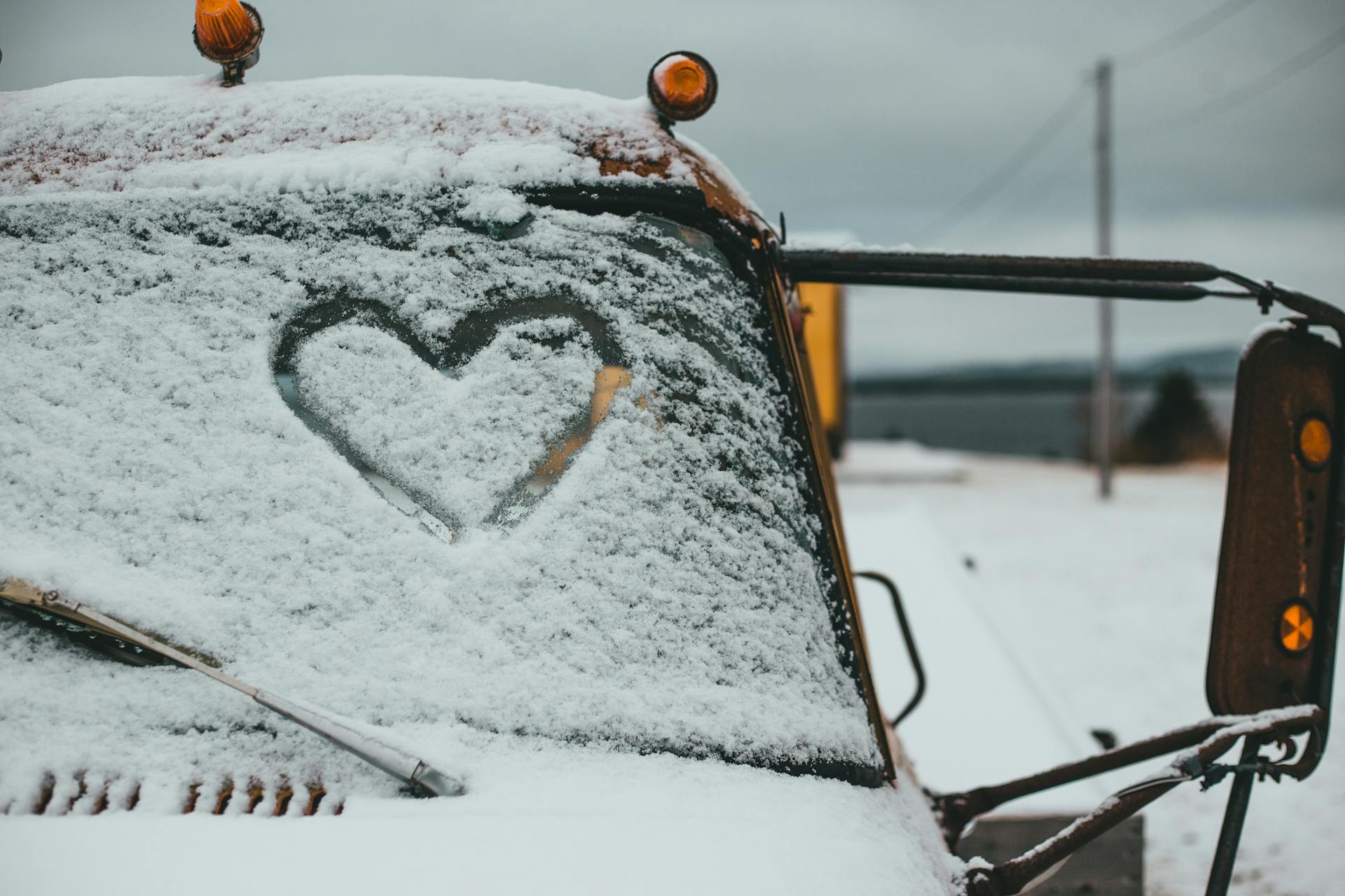 Finger drawn heart symbol on windshield of truck covered with hoarfrost parked on snowy terrain of waterside on winter day