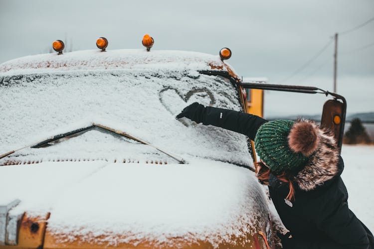 Unrecognizable Woman Drawing Heart On Snowy Windshield