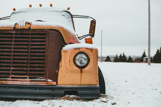 Yellow old timer truck with headlight covered with frost parked on snowy terrain against trees in rural terrain on winter day