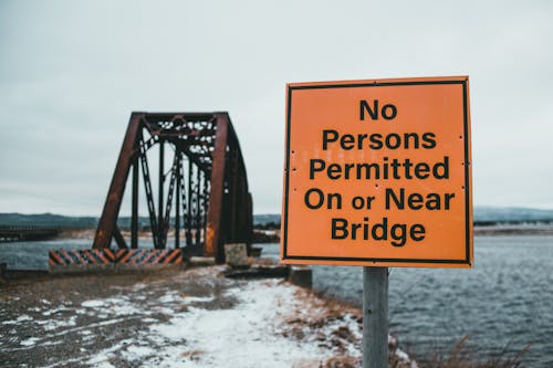 Restrictive signboard on snowy shore against bridge over sea
