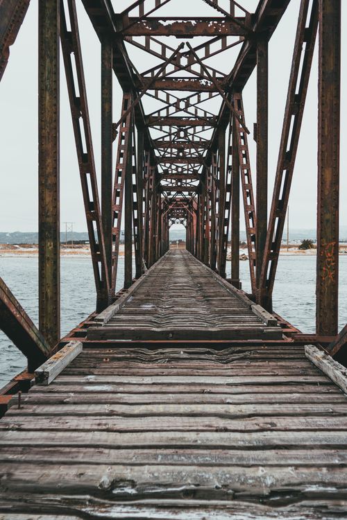 Free Old bridge with empty wooden pathway and metal fence with corrosion over ocean in daylight Stock Photo