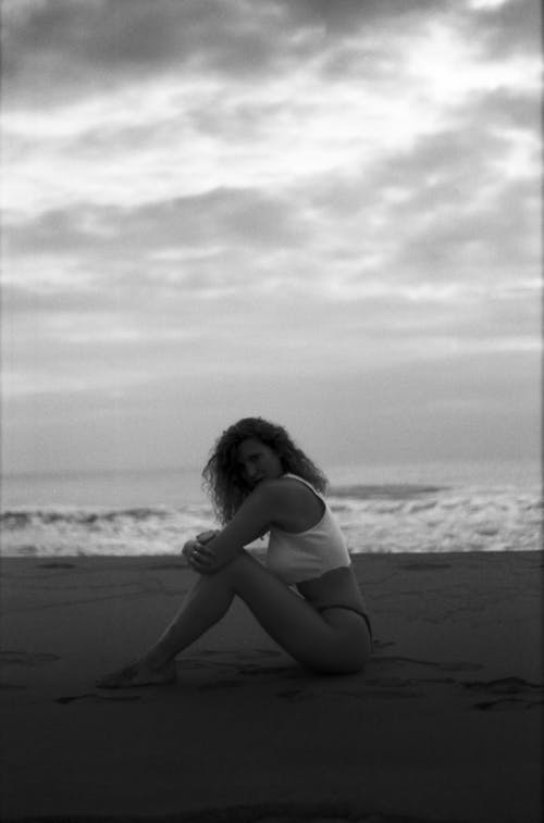 Grayscale Photo of a Woman Sitting on the Sand