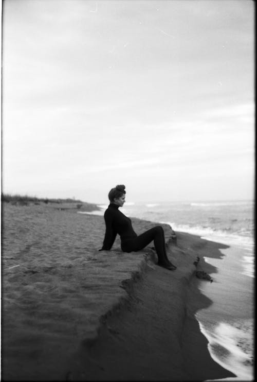 Grayscale Photo of a Woman Sitting on the Seashore