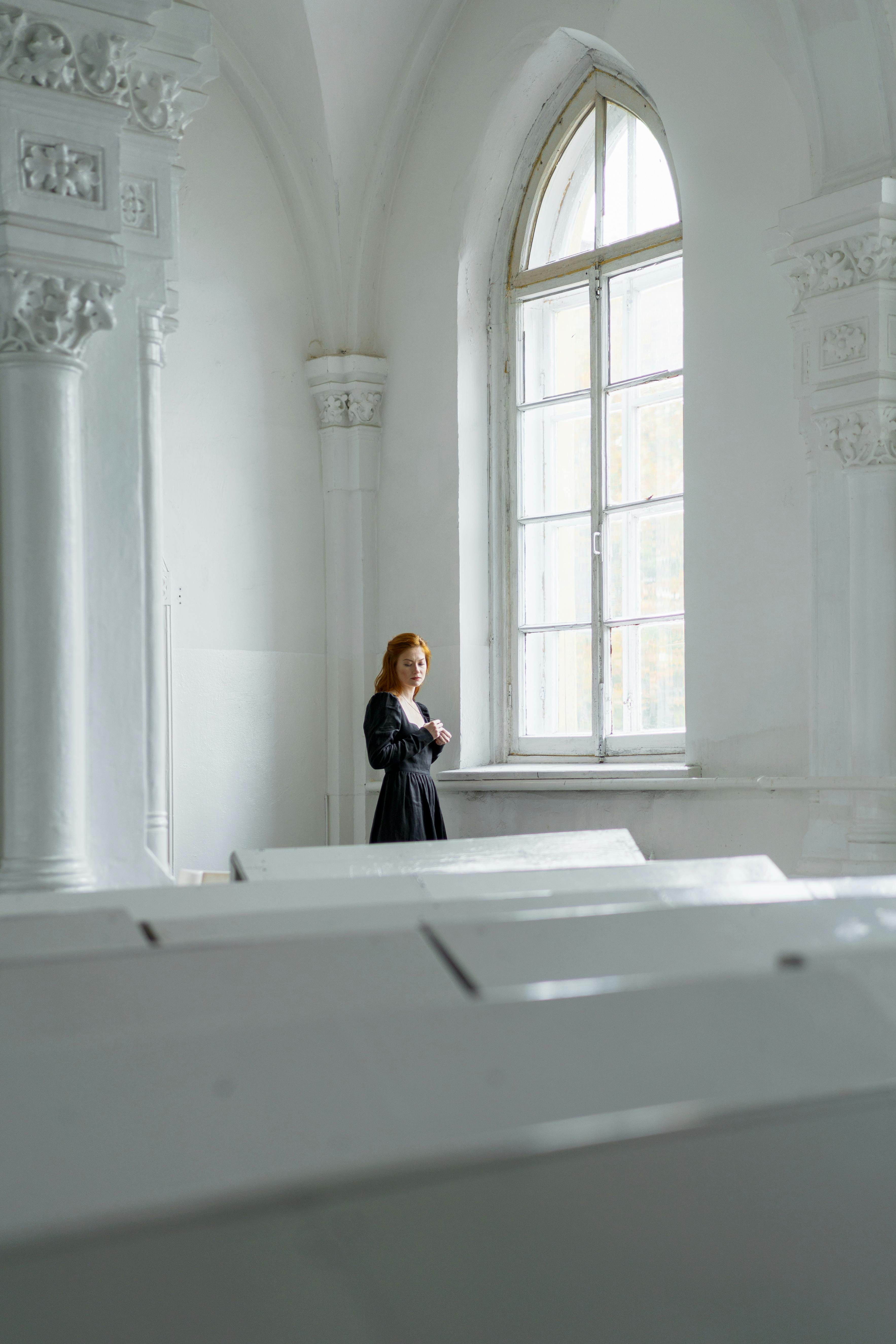 woman in black dress standing near the arched glass window