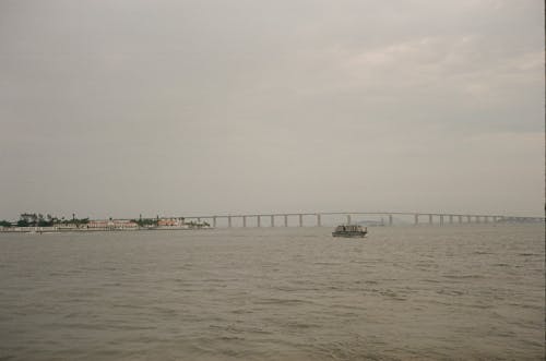 Picturesque scene of serene wide river small ship and long bridge in cloudy day