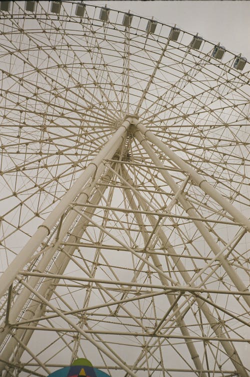 Low angle of huge Ferris wheel with cabins in amusement park against grey sky