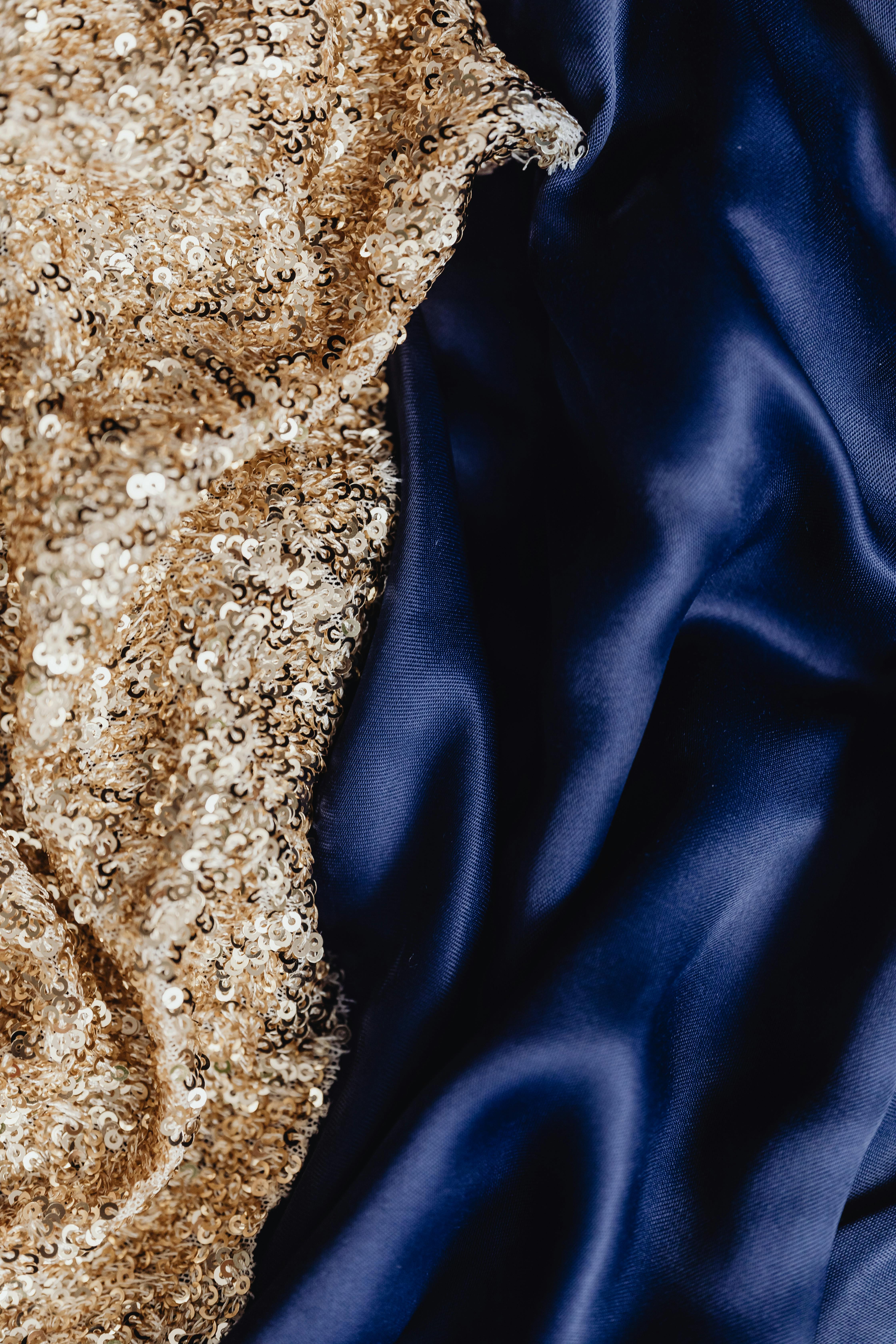 Close-up of shimmering gold sequins paired with dark blue satin fabric for a luxurious and elegant look.