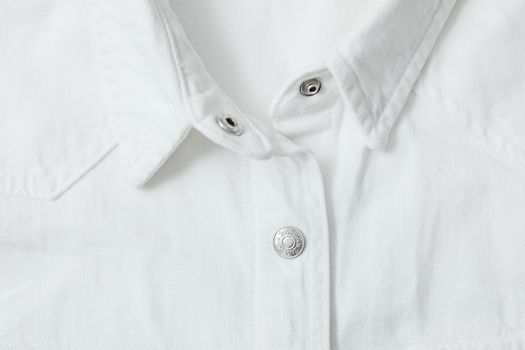 Detailed view of a white shirt with metal buttons and textured fabric.