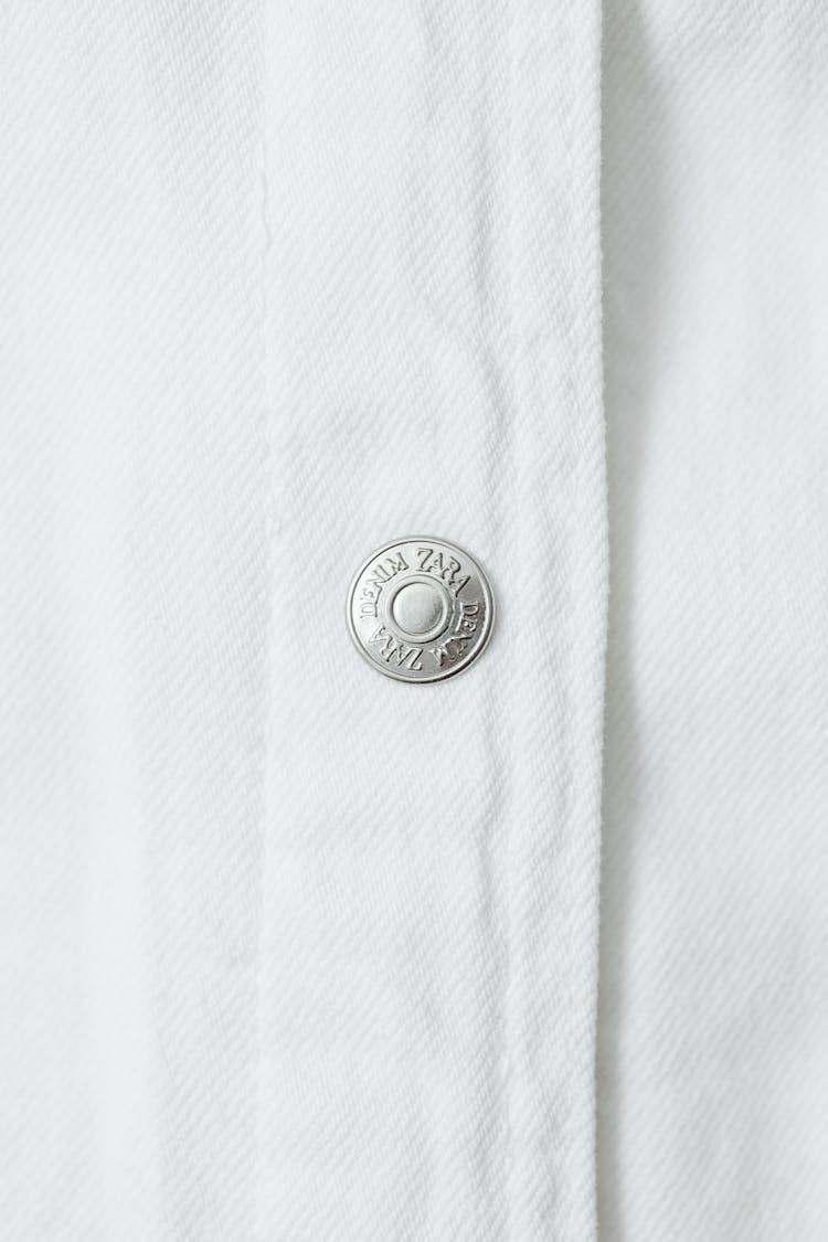 Close-Up Photo Of A Silver Button On A White Textile