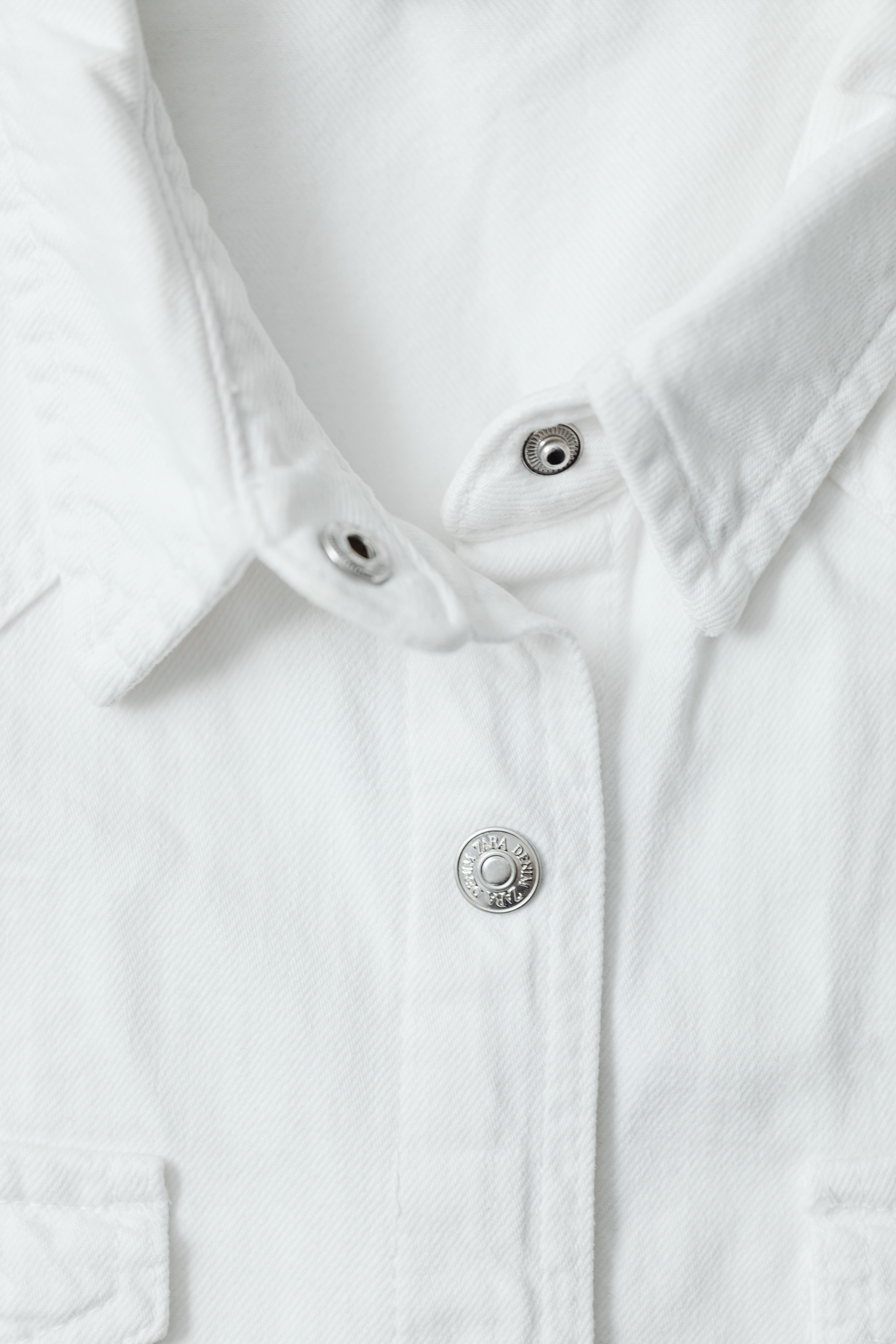 Close-up of a white button-up woven shirt showing the collar, placket and buttons for a shirt tech pack