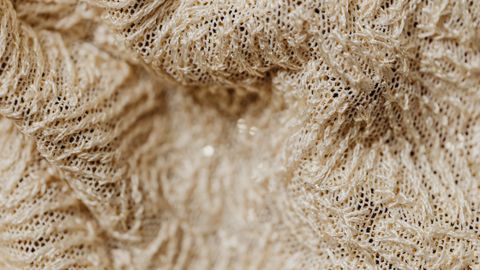 Detailed close-up of textured beige woven fabric with intricate fibers, ideal for textile and design concepts.