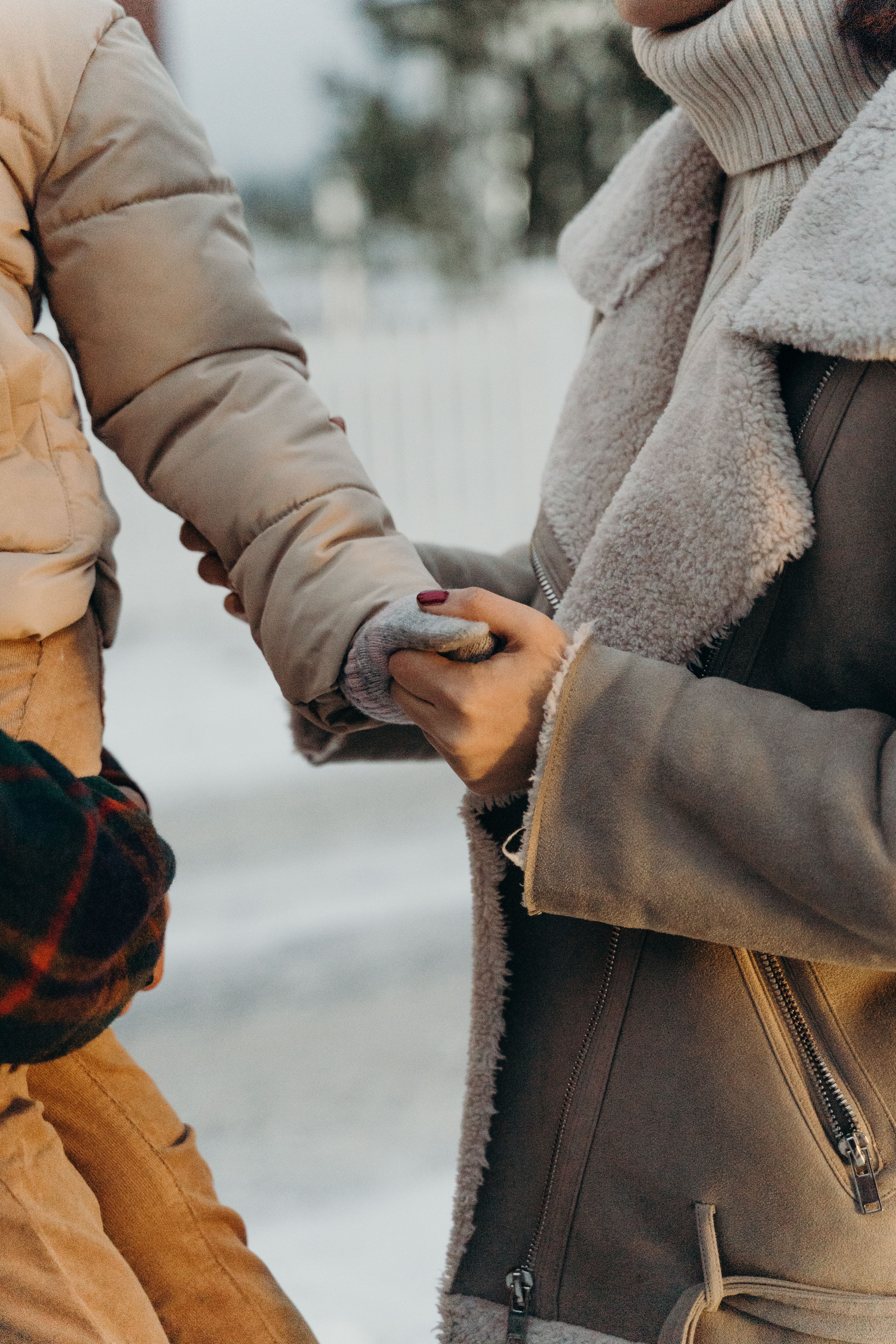 Close-up of a child and adult holding hands in warm winter clothing outdoors.