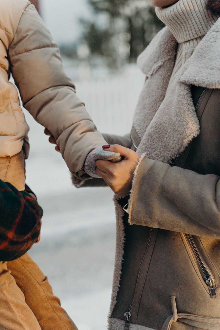 Close-up of a child and adult holding hands in warm winter clothing outdoors.