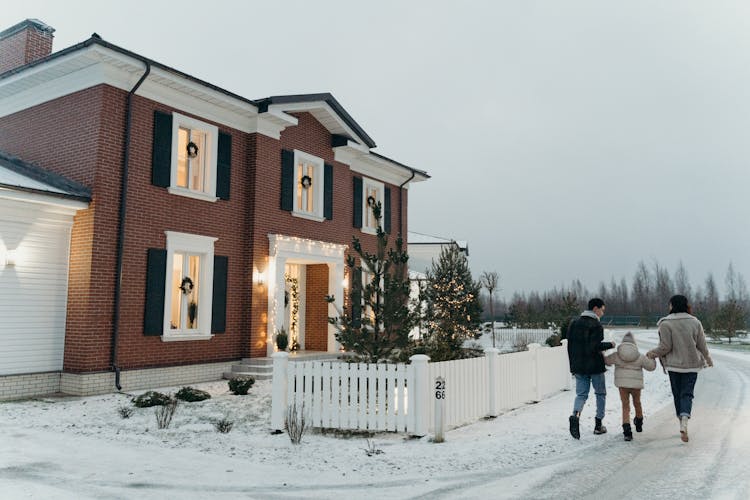 A Family Walking On Snow Covered Ground Near A Brick House