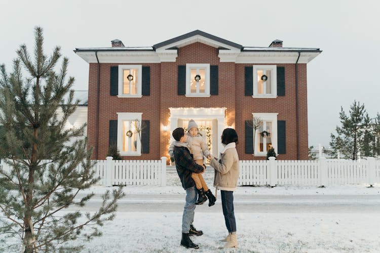 Couple With A Child In Front Of A House In Winter 