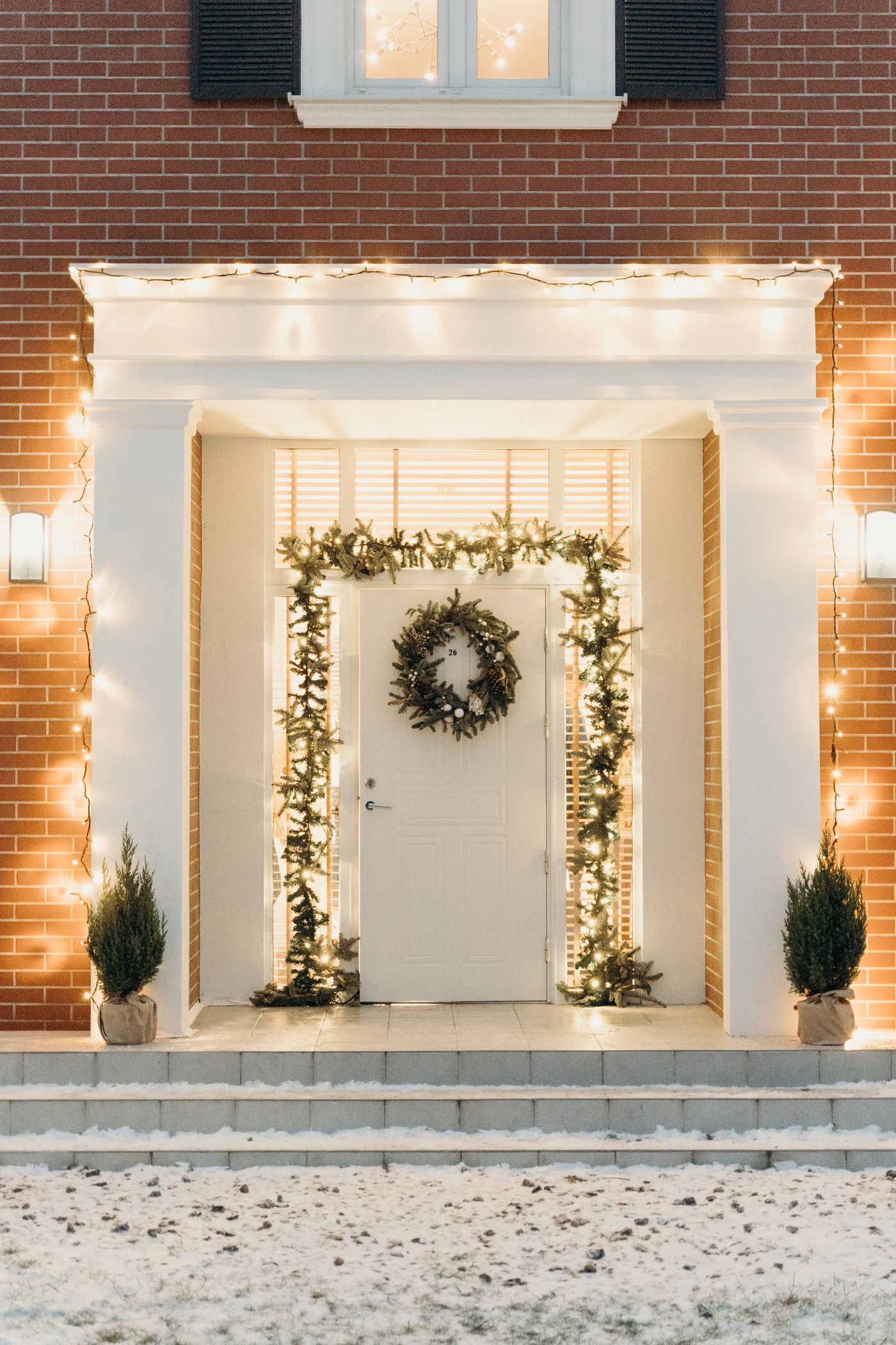 Porte d’entrée blanche décorée avec une couronne et des guirlandes lumineuses pour Noël