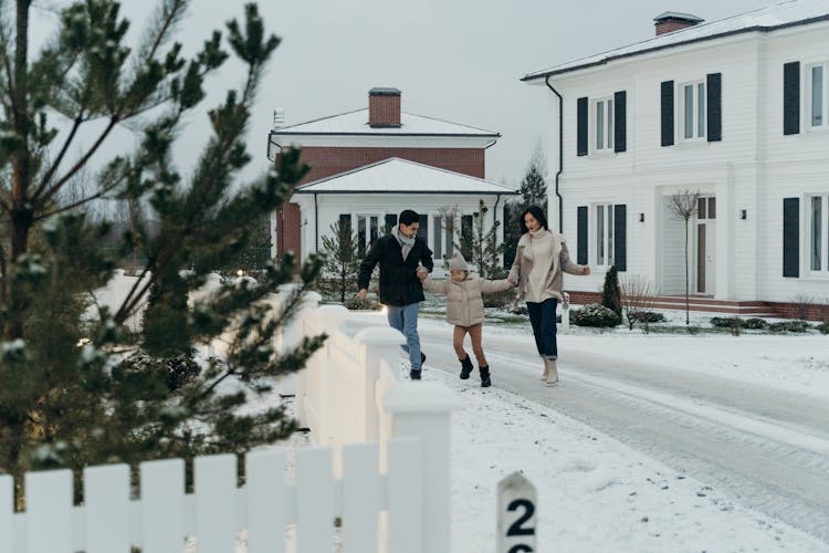 Family Standing On Snow Covered Ground Near White Wooden Fence