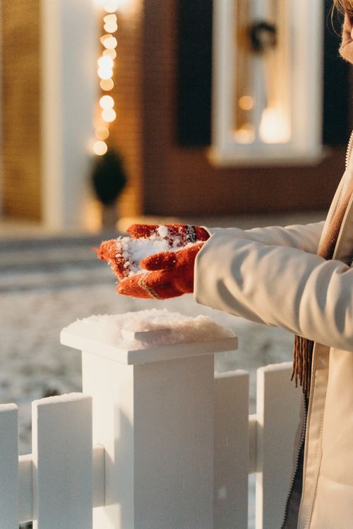 Free A woman holding fresh snow by a decorated home during a cozy winter evening. Stock Photo