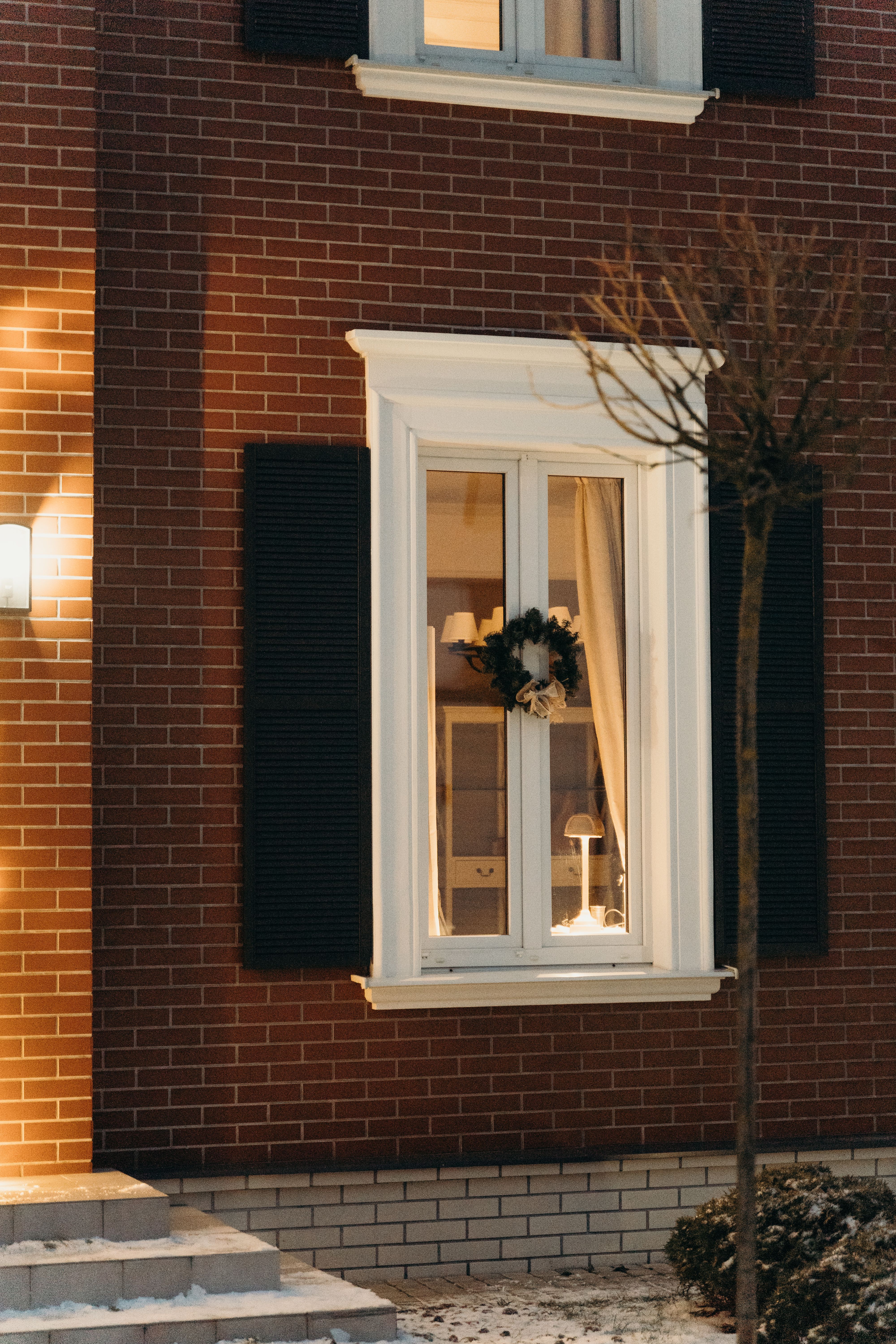 Warm exterior view of a brick house window adorned with a decorative wreath.