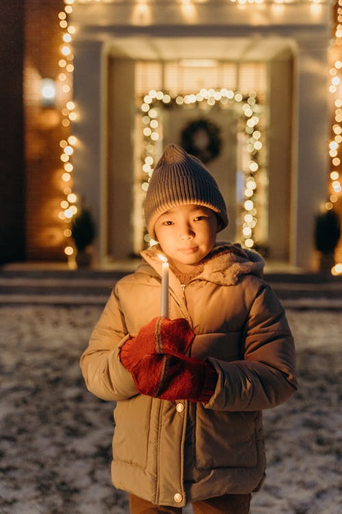 Photo of a Child in a Brown Puffer Jacket Holding a Lit Candle
