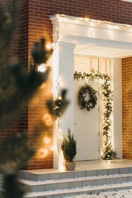 Elegant entrance decorated with a Christmas wreath and string lights on a brick house.