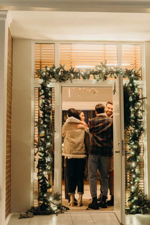 Free Warm holiday celebration with friends and family embracing in a decorated home doorway. Stock Photo