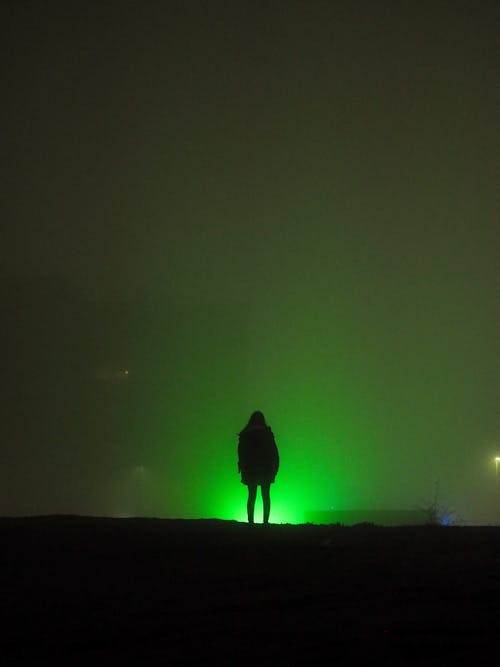 Silhouette of Person Standing on Hill With Green Light during Nighttime