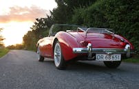 日落时分，一辆经典的红色敞篷车停在风景优美的路边，尽显奢华与时尚