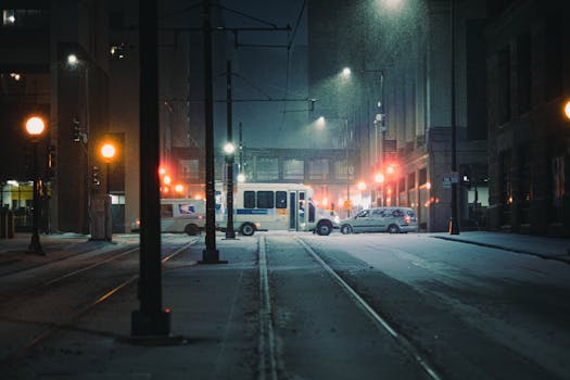 Snowfall on a quiet Saint Paul street at night with a tram passing by, illuminating the city lights.