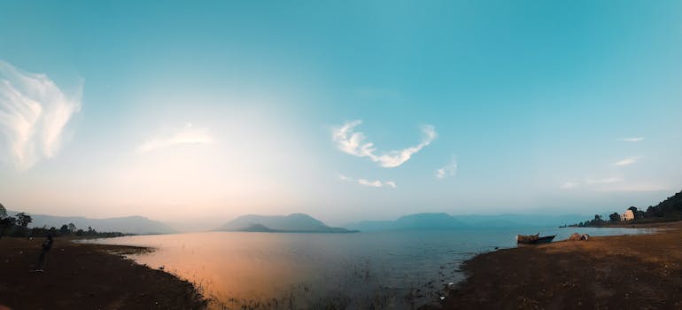 Panorama of seacoast near sea with boat against blue sky with clouds and hilly terrain in countryside on summer day