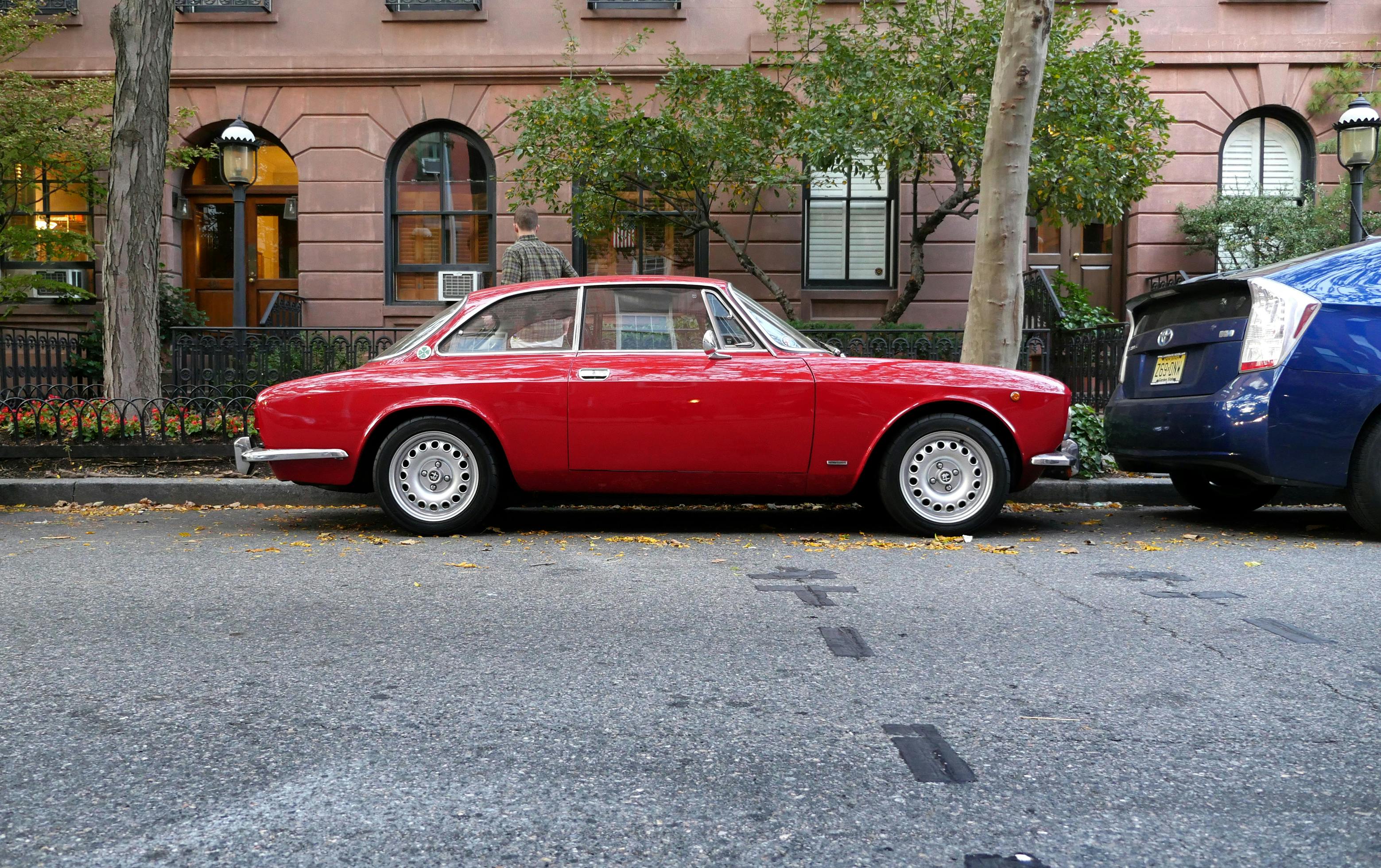 Classic Red Coupe Parked Near Blue Toyota Prius on Sidewalk