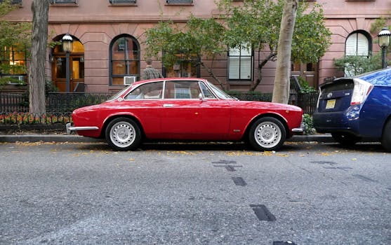 一辆经典的红色汽车停靠在城市街道上，背景是树木和建筑物