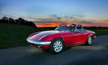 一辆经典的红色敞篷跑车停在道路上，背景是令人惊叹的日落