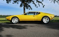 一辆黄色老式敞篷车停在阳光明媚的乡村公路上，展现出经典的设计