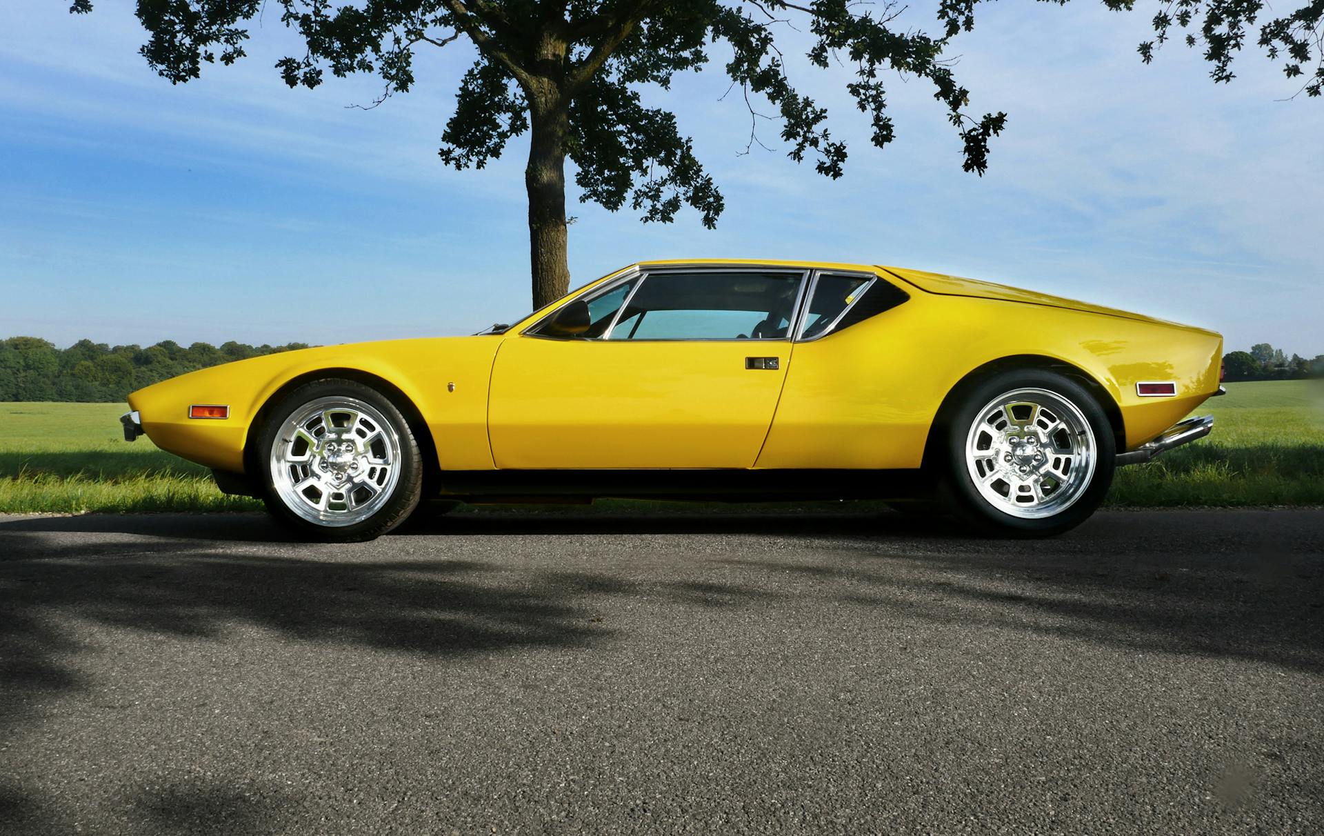 A vintage yellow convertible car parked on a sunny rural road, showcasing its classic design.