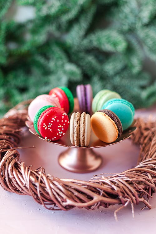 Sweet colorful macaroons served on bowl on white table near wooden wreath in living room