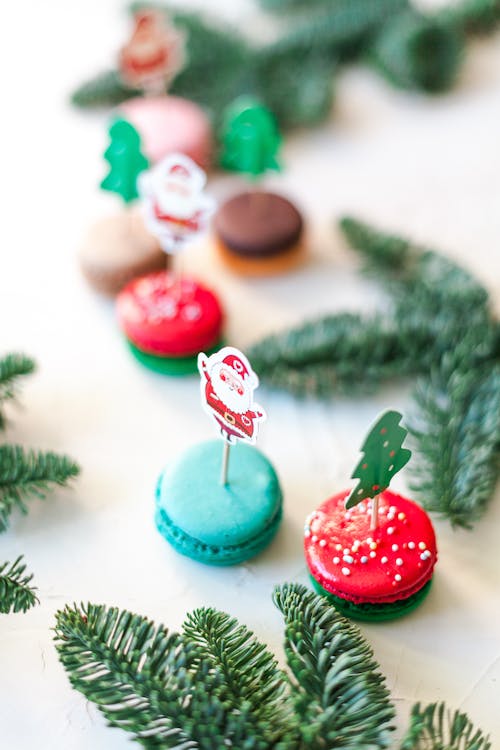 Free High angle composition of colorful sweet macaroons decorated with Santa Claus figures placed on white table near fir branches Stock Photo