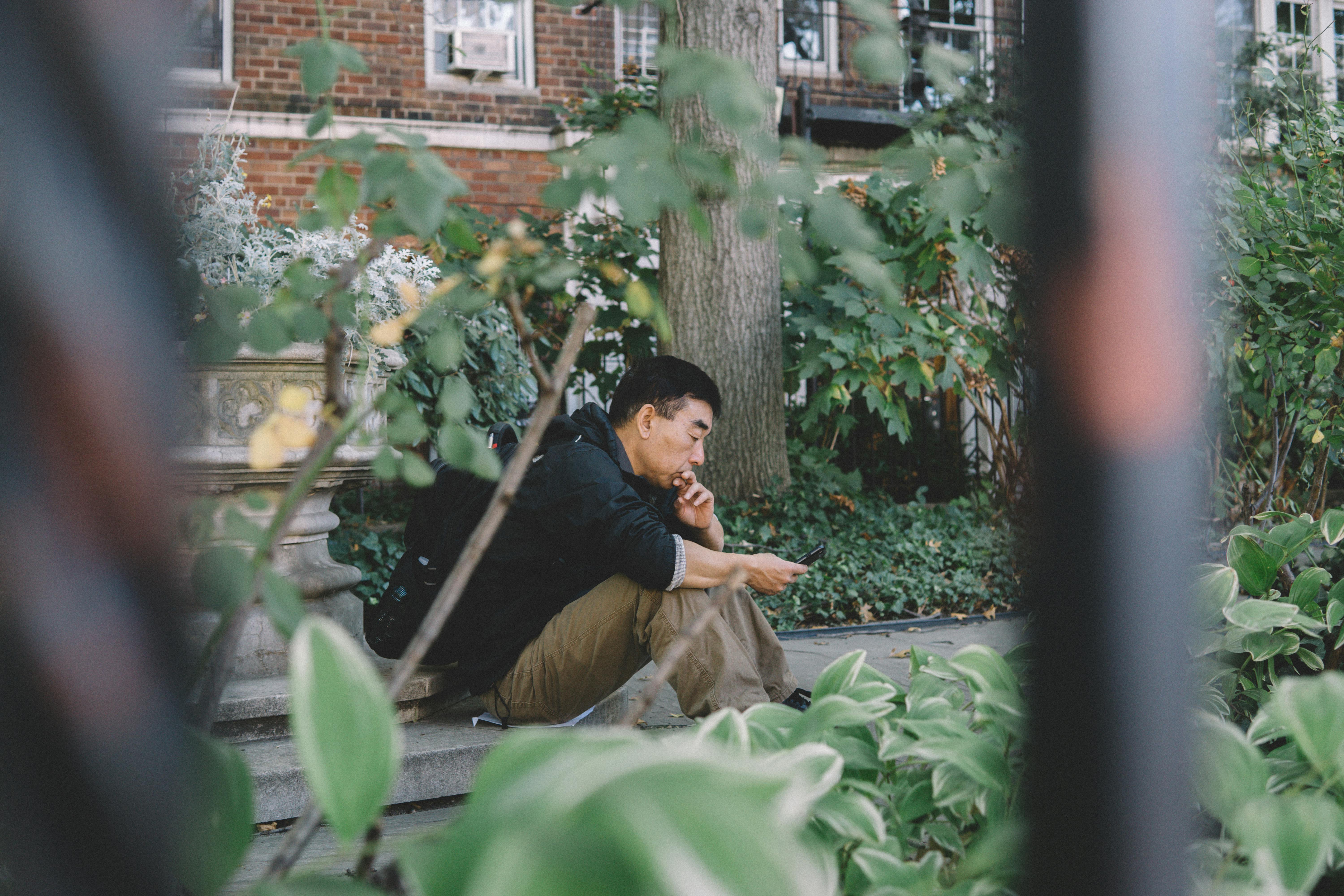 A young man using a smartphone while sitting in a lush urban garden setting.