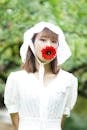 Photo of a Woman with a Red Barberton Daisy on Her Mouth
