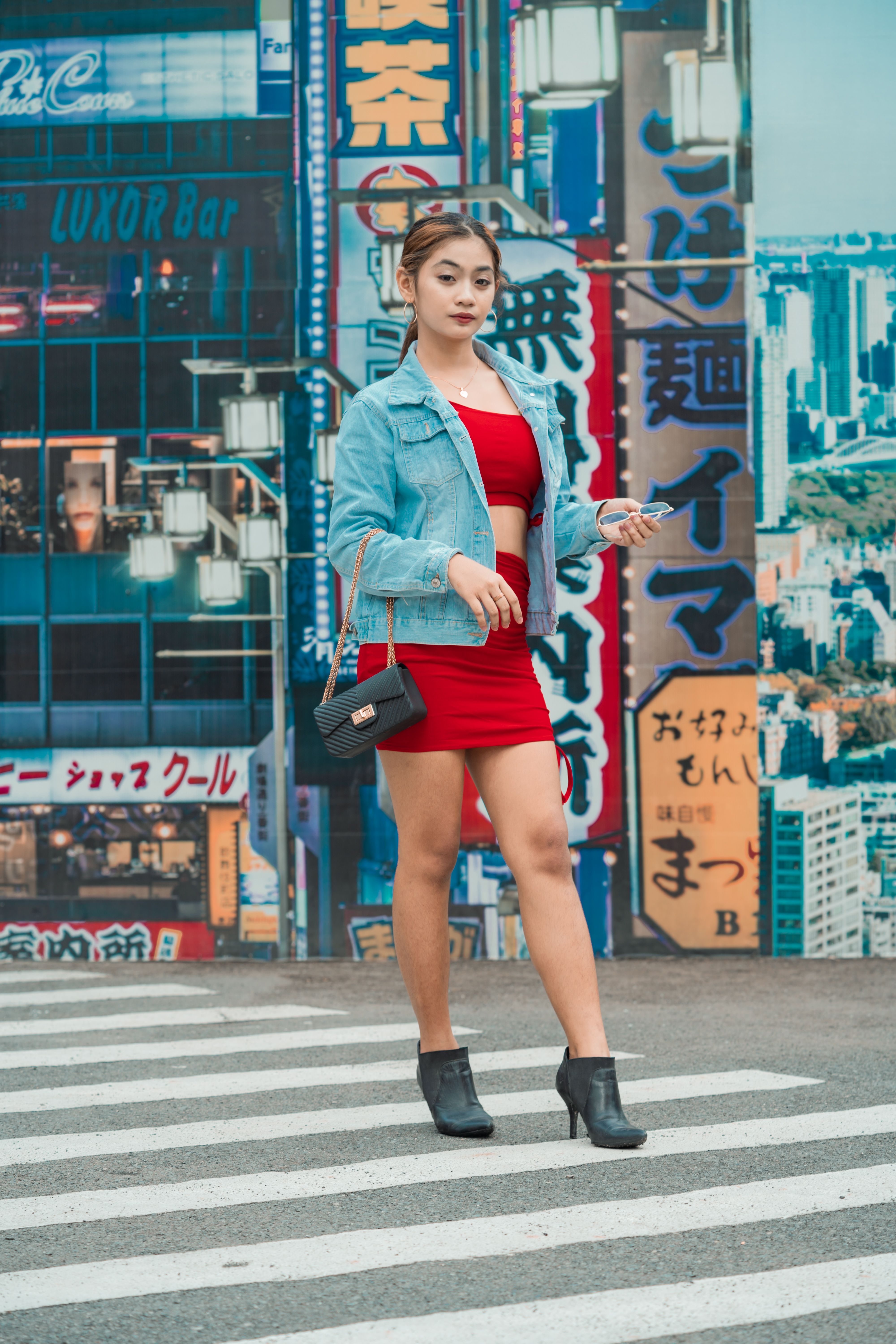 Stylish Asian woman in denim and red dress crossing a city street with Tokyo backdrop.