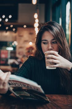 Asian woman relaxing with coffee and a book in a cozy, stylish cafe setting.